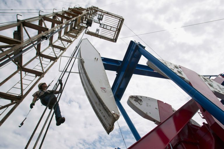 FILE - In this July 26, 2011, file photo, a worker hangs from an oil derrick outside of Williston, N.D. State data show that 1 billion barrels of oil have been produced from the rich Bakken shale formation in western North Dakota and eastern Montana. Data show that North Dakota has tallied 852 million barrels of Bakken crude, and Montana has produced about 151 million barrels. (AP Photo/Gregory Bull, File)
