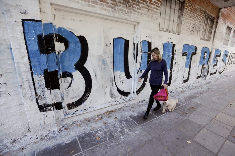 A woman walks with her dog past a mural that reads in Spanish 