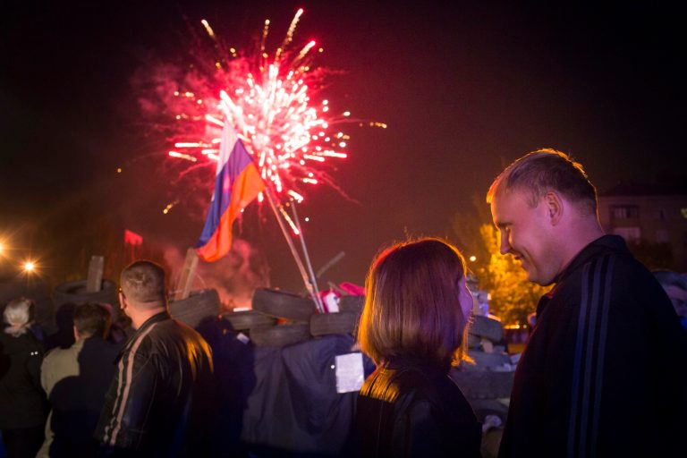 People watch fireworks celebrating the declaration of independence for Donetsk region at barricades in front of a regional administration building that was recently seized by pro-Russian activists in Donetsk, Ukraine, Monday, May 12, 2014, with a Russian national flag is in the background.  Pro-Moscow insurgents in eastern Ukraine declared independence Monday, putting pressure on Kiev to hold talks with the separatists. (AP Photo/Alexander Zemlianichenko)