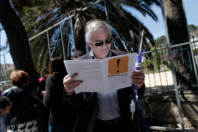 A Cypriot man reads a leaflet handed out by protesters at the end of a parade for Greek Independence Day celebrations in capital Nicosia, Cyprus, Monday, March 25, 2013. Cyprus secured what its politicians described as a 
