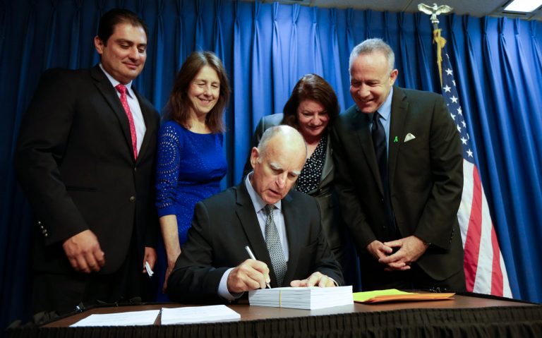 California Gov. Jerry Brown, center, signs the 2014-15 state budget Friday, June 20, 2014, in San Diego. Looking on behind are, from left, state Sen. Ben Hueso, state Assemblymember Nancy Skinner, state Assembly Speaker Toni Atkins, and state Senate Leader Darrell Steinberg. Brown signed California's $108 billion general fund spending plan Friday, which sets aside money in a rainy day fund and pays down state debts thanks to surging tax revenue and the booming stock market. (AP Photo/Gregory Bull)