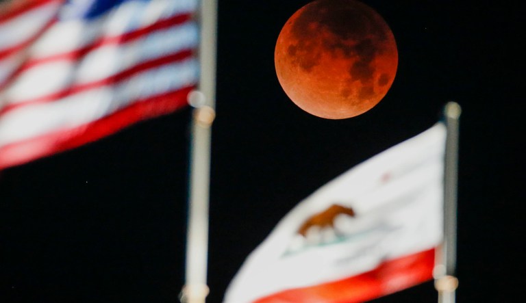 A rare occurrence called a Super Blue Blood Moon is seen behind the flags of U.S. and California state at Santa Monica Beach in Santa Monica, Calif., Wednesday, Jan. 31, 2018.