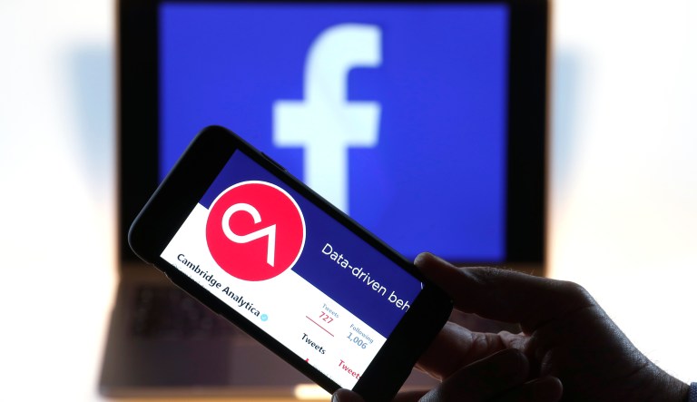 The verified Twitter Inc. page of Cambridge Analytica, displaying their logo and company name, sit on an Apple Inc. iPhone against a backdrop of the Facebook Inc. sign shown on a computer screen in this arranged photograph in London, U.K., on Thursday, March 22, 2018. Facebook Inc.âs co-founder and chief executive officer Mark Zuckerberg has been called to appear before a House panel as fallout continues from revelations that Cambridge Analytica had siphoned data from some 50 million Facebook users as it built a election-consulting company that boasted it could sway voters in contests all over the world.