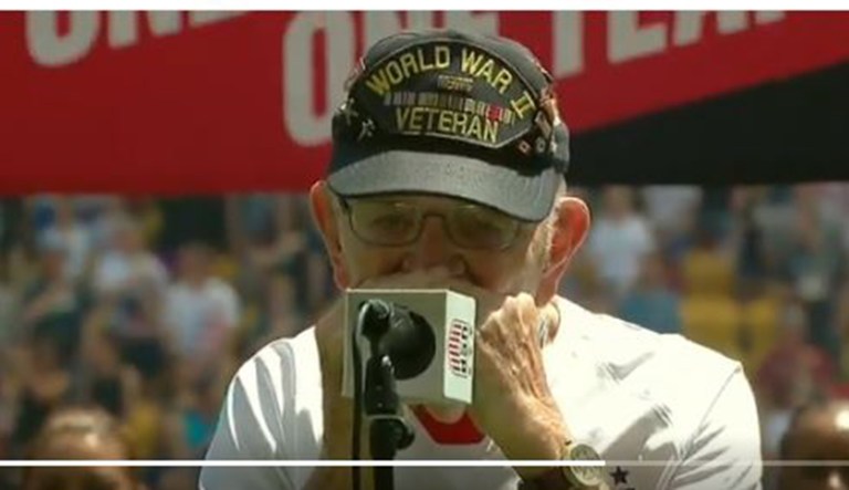Pete Dupre plays the U.S. national anthem on a harmonica before the beginning of a soccer game.
