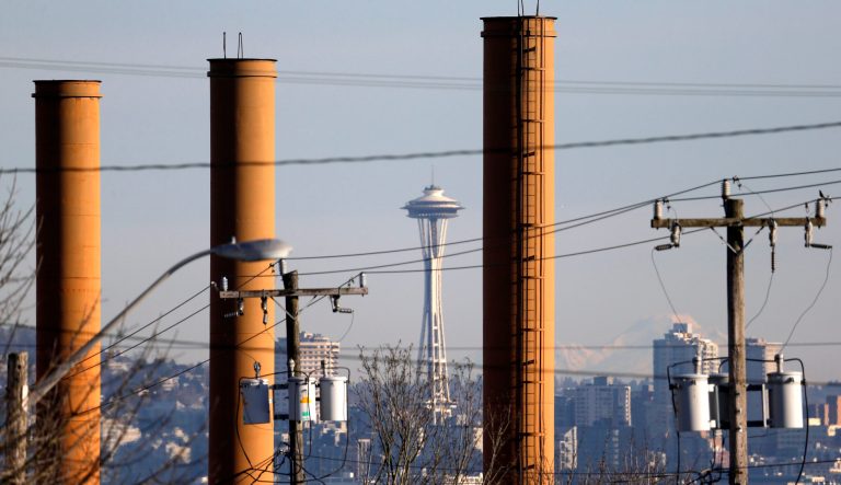 In this Feb. 25, 2016, file photo the Space Needle is seen in view of still-standing but now defunct stacks at the Nucor Steel plant in Seattle.