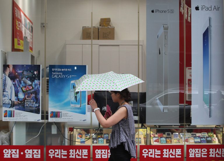 A woman walks by advertisement posters of Samsung Electronics' Galaxy S5, Apple's iPhone 5s and iPad Air at a mobile phone shop in Seoul, South Korea, Wednesday, Aug. 6, 2014. Samsung and Apple Inc. have agreed to end all patent lawsuits between each other outside the U.S. in a step back from three years of legal hostilities between the world's two largest smartphone makers. (AP Photo/Ahn Young-joon)