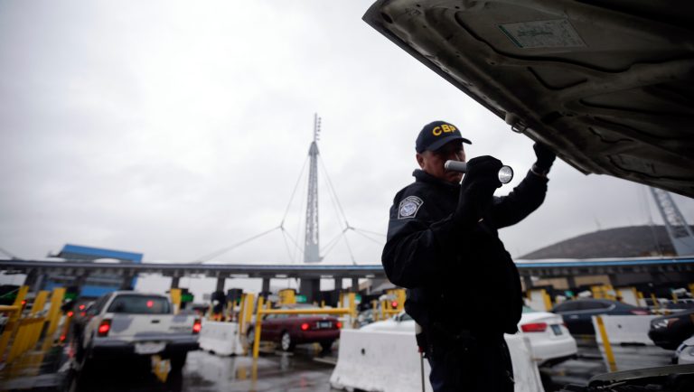 FILE - In this Dec. 3, 2014 file photo, a U.S. Customs and Border Protection (CBP) officer checks under the hood of a car as it waits to enter the U.S. from Tijuana, Mexico through the San Ysidro port of entry in San Diego. A group of First Amendment attorneys is suing the Trump administration over access to data showing how often citizens and visitors had their electronic devices searched and the contents catalogued at the border. 