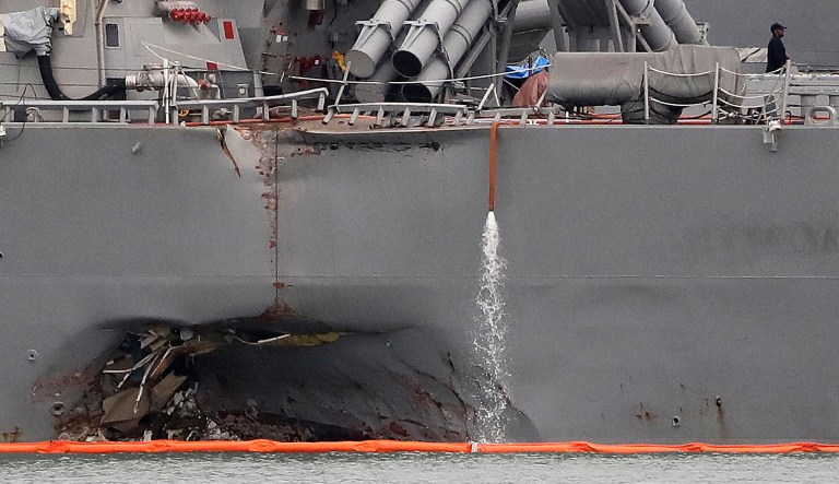 The damaged port aft hull of the USS John S. McCain, is visible while docked at Singapore's Changi naval base on Tuesday, Aug. 22, 2017 in Singapore. Cmdr. Jessie Sanchez, former commander of the USS John S. McCain, as well as Cmdr. Bryce Benson, former commander of the USS Fitzgerald, are facing charges related to their respective collisions with merchant ships. (AP Photo/Wong Maye-E)