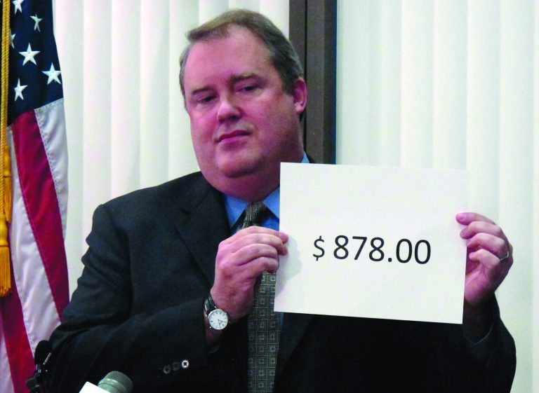 Alaska Revenue Commissioner Bryan Butcher holds up the amount of this year's Permanent Fund Dividend during a news conference Tuesday, Sept. 18, 2012, in Anchorage, Alaska. Butcher announced this year's check from the state's oil riches will be $878 for nearly every single Alaskan. (AP Photo/Mark Thiessen)