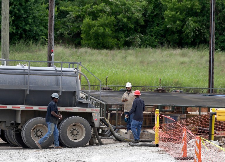 Workers use hoses to to empty fluid out of their tractor trailers into a holding tank, at right, at an XTO Energy Inc. well site, Saturday, June 21, 2014, in Azle, Texas. (AP Photo)Â 