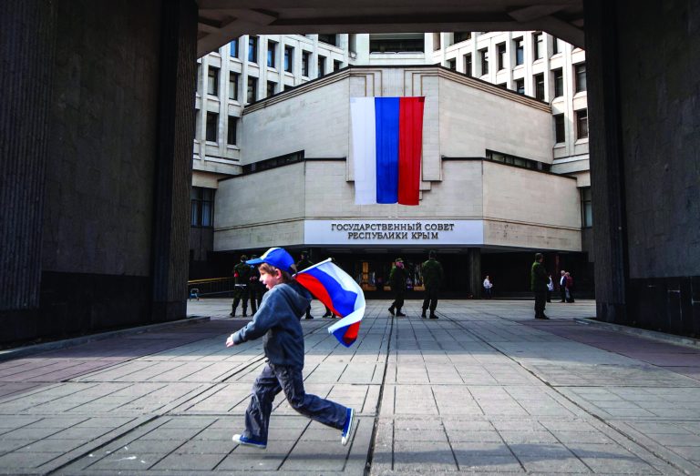 A boy runs with a Russian national flag at the Crimean parliament in Simferopol, Crimea, Wednesday. Within days of Crimea being swallowed up by Russia, the lights began flickering out. (AP Photo/Alexander Polegenko)