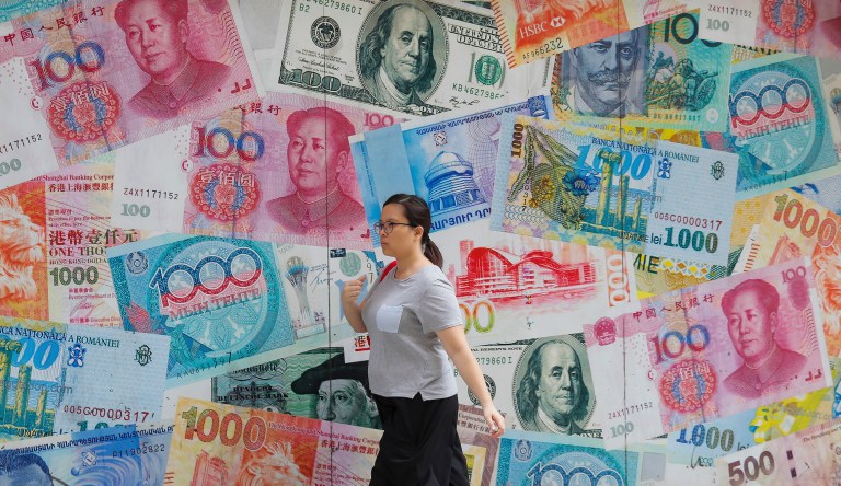 A woman walks by a money exchange shop decorated with different countries currency banknotes at Central, a business district in Hong Kong, Tuesday, Aug. 6, 2019. 