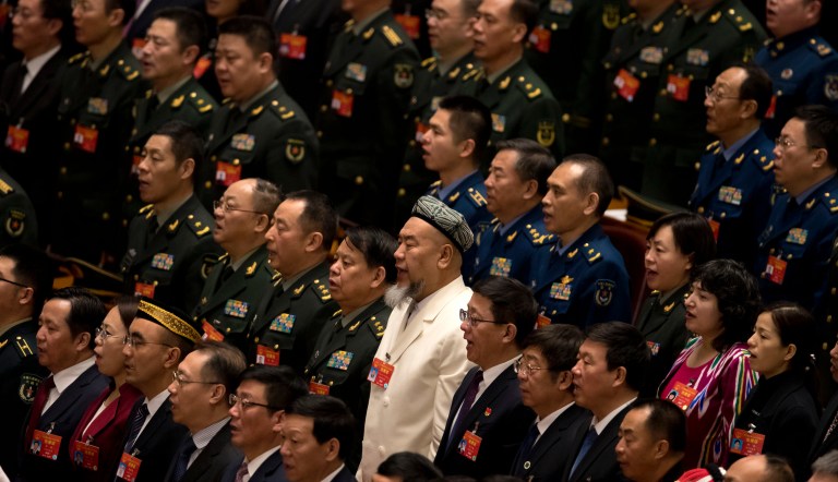 A delegate in traditional Uighur dress, bottom center, stands with military delegates as they sing the Chinese national anthem during the closing session of China's National People's Congress (NPC) at the Great Hall of the People in Beijing, Friday, March 15, 2019. 