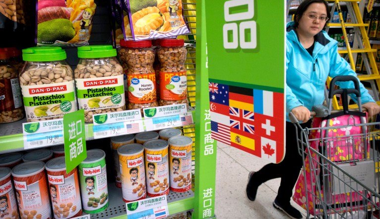 FILE - In this March 23, 2018. file photo, a woman pushes a shopping cart past a display of nuts imported from the United States at a supermarket in Beijing. China raised import duties on a $3 billion list of U.S. pork, fruit and other products Monday, April 2, 2018 in an escalating tariff dispute with President Donald Trump that companies worry might depress global commerce.