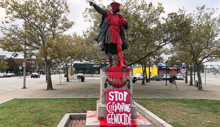 A sign reading "stop celebrating genocide" sits at the base of a statue of Christopher Columbus on Monday, Oct. 14, 2019, in Providence, R.I., after it was vandalized with red paint on the day named to honor him as one of the first Europeans to reach the New World.