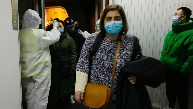 Health Officials in hazmat suits check body temperatures of passengers arriving from the city of Wuhan Wednesday, Jan. 22, 2020, at the airport in Beijing, China. 