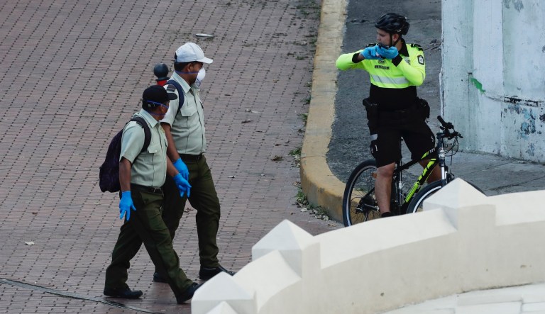 Two private security agents wearing mask and gloves as a precaution against the spread of the new coronavirus exchange words with a police officer, just before the start of curfew, at the Casco Viejo neighborhood of Panama City, Tuesday, March 24, 2020. Panamanian President Laurentino Cortizo announced the change of a partial curfew to a full day curfew in all the country to help slow the spread of COVID-19.