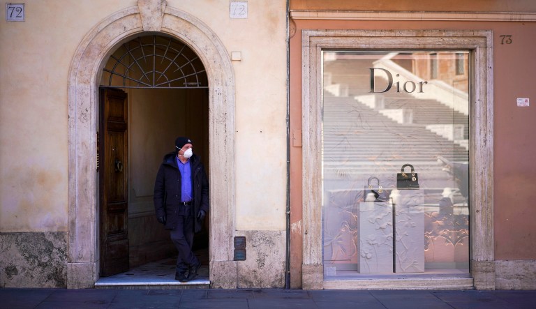 A man with a face mask stands near a closed luxury shop in Rome, Thursday, March 12, 2020.