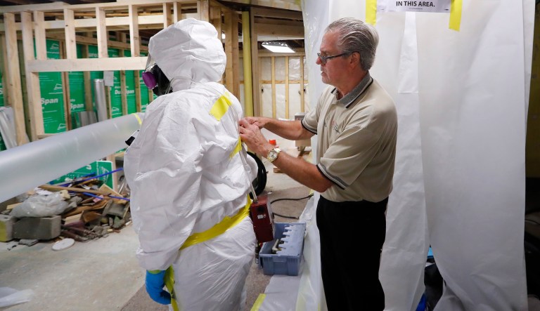 George Riegel, Jr., M.D., right,  owner of Asbestos Removal Technologies Inc., helps prepare a personal air monitor on job forman Megan Eberhart before asbestos abatement in Howell, Mich., Wednesday, July 12, 2017.