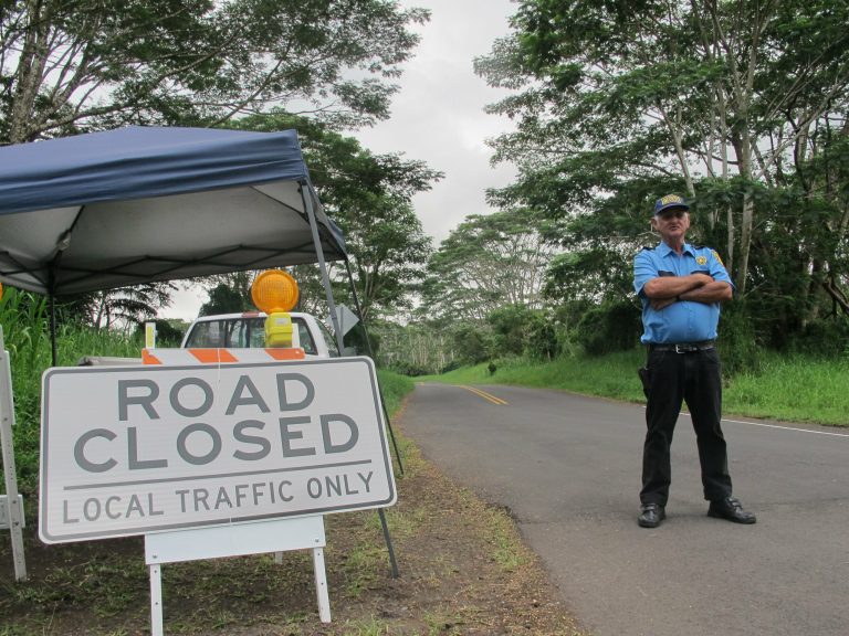 In this Monday, Sept. 8, 2014 photo, security guard George Cortez stands at a roadblock to prevent non-residents from entering the lava-threatened community of Kaohe Homesteads in Pahoa, Hawaii. Those who live on the slopes of Kilauea volcano know lava could start creeping their way at any time but the area is still a powerful draw for many people who value its community and affordability. (AP Photo/Audrey McAvoy)