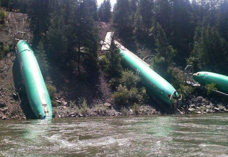 This Sunday, July 6, 2014 photo by Jerry Compton provided by Wiley E. Waters Whitewater Rafting shows a freight train that derailed near Alberton in western Montana, sending three cars carrying aircraft components down a steep embankment and into the Clark Fork River on Thursday, July 3. Removing three Boeing 737 fuselages could take until Tuesday. Montana Rail Link spokeswoman Lynda Frost said a crew of 50 with eight heavy equipment machines is working in conjunction on the steep bank. (AP Photo/Wiley E. Waters Whitewater Rafting, Jerry Compton)