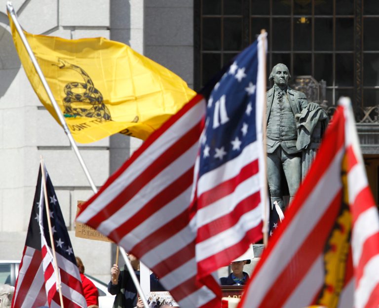 A statue of George Washington is seen amidst American flags adn the Tea Party flag during a rally at the Capitol in Albany, N.Y., on Tuesday, April 13, 2010. (AP Photo/Mike Groll)