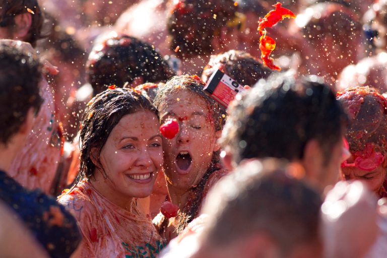 A tomato is about to hit two women taking a selfie during a tomato fight in front of the Royal Palace turning Amsterdam's central Dam square into a red pulpy mess Sunday, Sept. 14, 2014. Entrepreneurs have seized upon Russia's boycott of European produce to set up a tomato-throwing fight. The idea is lifted from Spain's famed annual 