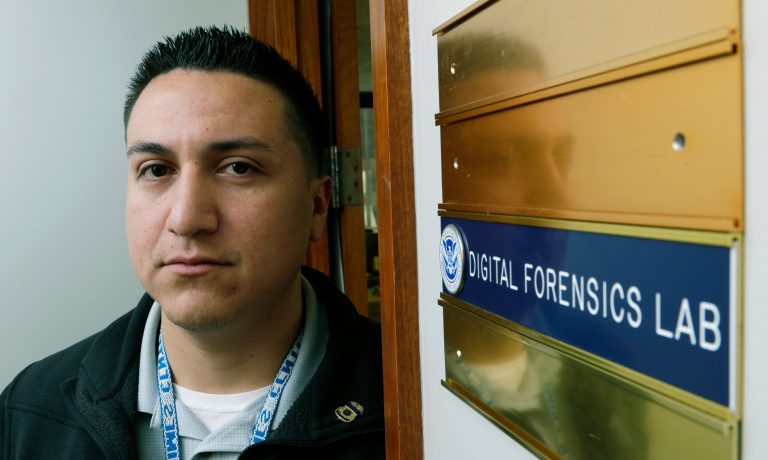 In this Monday, Dec. 16, 2013, photo, Army Staff Sgt. Oskar Zepeda poses for a photo at the entrance to a Digital Forensics Lab at an  Immigration and Customs Enforcement field office in Seattle, where he is serving a one-year internship. Zepeda, who served nine tours of duty in Iraq and Afghanistan, before being wounded, is part of a 17-member class of veterans deployed to ICE field offices throughout the country to use his newly acquired skills in computer forensics to help capture and prosecute child predators. (AP Photo/Ted S. Warren)