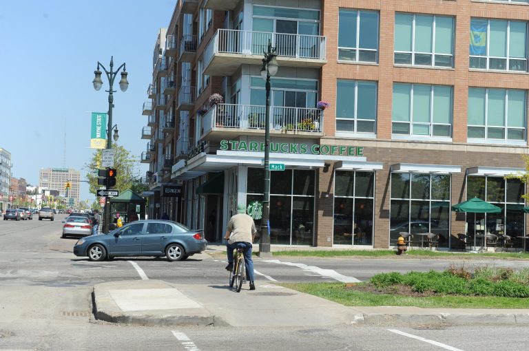 A cyclist stops at the corner where one of the many stops for the M-1 Rail is planned at Woodward Avenue and Mack Avenue in Detroit on Monday, May 19, 2014.  Officials say Detroit's $140 million light passenger rail project is moving forward toward an expected summer groundbreaking. Officials haven't said exactly when the groundbreaking will take place. Below-ground utility relocation began late last year for the 3.3-mile project. The streetcar line is to start running along Detroit's Woodward Avenue in 2016. (AP Photo/Detroit News, Max Ortiz)  DETROIT FREE PRESS OUT; HUFFINGTON POST OUT