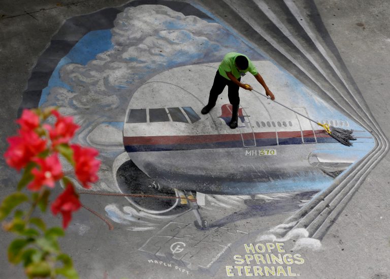 FILE - In this April 8, 2014, file photo a school utility worker mops a mural depicting the missing Malaysia Airlines Flight 370 at the Benigno 