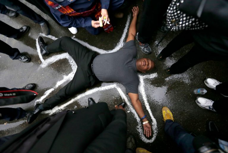 Pastor Charles Burton lies on the driveway at the Ferguson, Mo., police station as a chalk drawing is made as a memorial to Michael Brown, Monday, Oct. 13, 2014. (AP/Charles Rex Arbogast)