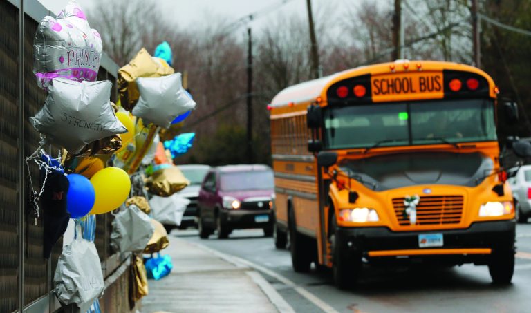 FILE - In this Dec. 18, 2012 file photo, a school bus rolls toward a memorial in Newtown, Conn., for victims of the Sandy Hook Elementary School shooting. Nearly three weeks after the shooting rampage, classes are starting Thursday, Jan. 3, 2013 for the Sandy Hook students at a repurposed school in the neighboring town of Monroe, where the students' desks have been taken along with backpacks and other belongings that were left behind in the chaos following the shooting on Dec. 14. (AP Photo/Charles Krupa, File)