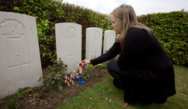 ADVANCE FOR SUNDAY JUNE 15 2014 TO  GO WITH STORY WWI-THE GREAT WAR -In this Thursday, April 24, 2014 photo, Kaylene Biggs, great-granddaughter of World War I Australian soldier Andrew Bayne, places a wooden cross with a poppy and a message on the grave at Westhof Farm Commonwealth Cemetery in Nieuwkerke, Belgium on Thursday, April 24, 2014. Bayne's grave lies among the 131 Commonwealth soldiers and a handful of German soldiers in this small cemetery surrounded by a landscape still scarred by countless bomb craters, rusting gas shells, bunkers and trenches. (AP Photo/Virginia Mayo)