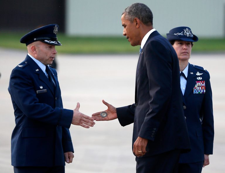 President Barack Obama presents a presidential challenge coin to U.S. Air Force Col. Douglas Mellars, left, accompanied by U.S. Air Force Col. Angela Cadwell, as he arrives at Royal Air Force Station Fairford,  Wednesday, Sept. 3, 2014, to attend the NATO Summit in Wales. (AP Photo/Charles Dharapak)