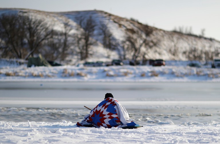 A man sits along the Cannonball river at the Oceti Sakowin camp where people have gathered to protest the Dakota Access oil pipeline. (AP Photo/David Goldman)