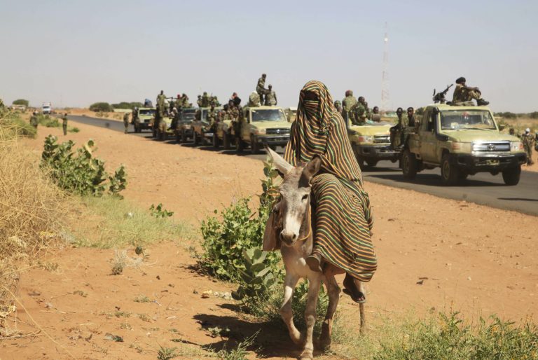 In this Thursday, Nov. 20, 2014 photo taken on a government organized media tour, a woman rides a donkey past a convoy of government troops in Tabit village in the North Darfur region of Sudan. (AP Photo/Abd Raouf)