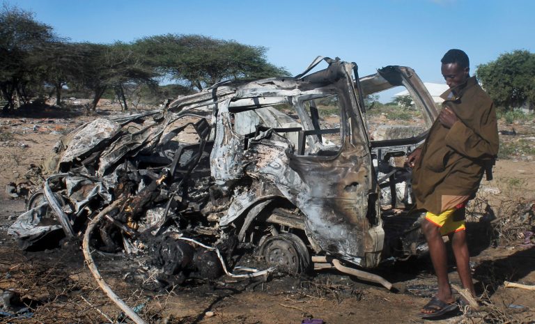 A Somali soldier stands near the wreckage of civilian vehicle destroyed by a suicide car bomb attack near the Elasha Biyaha settlement, in the Lower Shabelle region south of the capital Mogadishu, Somalia Monday, Sept. 8, 2014. At least 12 civilians were killed Monday when a suicide bomber detonated his explosives-laden car next to a convoy of African Union forces moving near two minibuses, followed by a second suicide attacker ramming his car into a convoy escorting the Mogadishu intelligence commander on his way to inspect the scene of the first blast, the first serious assault by suspected Islamic extremists after the killing of al-Shabab's top leader in a U.S. airstrike last week, according to a police and a regional official. (AP Photo/Farah Abdi Warsameh)