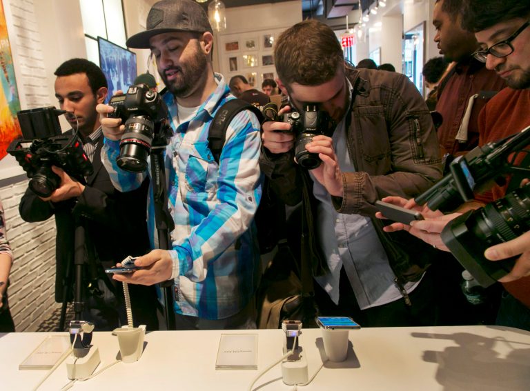 Photographers swarm around a Samsung Galaxy S5 smartphones, left,  and Samsung Gear 2's at the Samsung Galaxy Studio, in New York,  Monday, Feb. 24, 2014. Samsung on Monday unveiled a new smartphone with a built-in heart rate monitor to complement three upcoming fitness devices, as the Korean companies tries to turn its technological wizardry into lifestyle product. (AP Photo/Richard Drew)