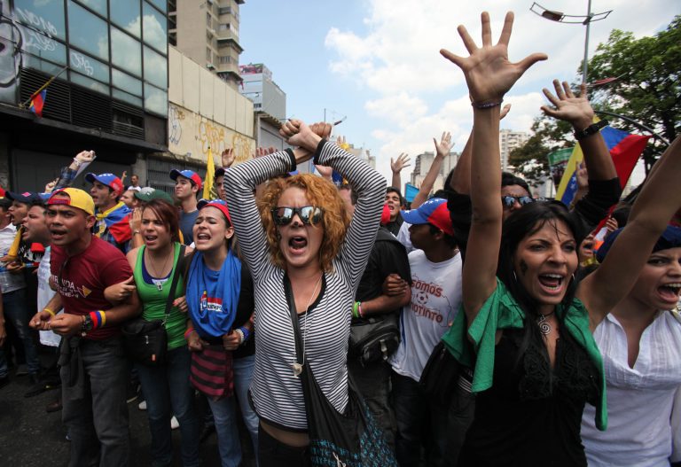 Opposition students shouts slogans against supporters of Venezuela's late President Hugo Chavez as they are blocked by police from reaching the electoral commission, to keep them and Chavez supporters separated, in Caracas, Venezuela, Thursday, March 21, 2013. The students were asking that the commission eliminate requirements that voters have their fingerprints recorded before voting. They were also demanding the government not interfere in politics ahead of an April 14 vote to replace Chavez. (AP Photo/Fernando Llano)