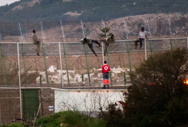 Four sub-Saharan migrants climb over a metallic fence that divides Morocco and the Spanish enclave of Melilla, as a Red Cross worker is on-hand to offer humanitarian assistance, Monday Feb. 17, 2014. A Spanish official says about 200 sub-Saharan migrants stormed a barbed-wire border fence along Spain's northwest African enclave of Melilla, with about 50 of them making it over. A spokesman for the Interior Ministry's office in Melilla said the melee began early Monday. The Spanish city of Melilla lies on the African continent, surrounded by Morocco and the Mediterranean Sea. Migrants hoping to get to Europe camp on the Moroccan side, with several thousand trying each year to enter the city and Spain's other coastal enclave of Ceuta.  (AP Photo/ Jesus Blasco de Avellaneda)