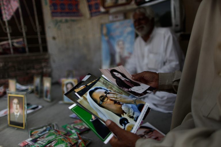 A Pakistani man looks at photographs of Pakistan's slain leader Benazir Bhutto, while displayed for sale by vendor, Mohammed Ashraf, 65, at the site where she was killed, in Rawalpindi, Pakistan, Monday, April 8, 2013. Pakistan's top court on Monday ordered former military ruler Gen. Pervez Musharraf to respond to allegations that he committed treason while in power and barred him from leaving the country. The Taliban have threatened to kill him, and he faces a series of legal charges that he has denied, including some related to the 2007 assassination of former Prime Minister Benazir Bhutto. (AP Photo/Muhammed Muheisen)