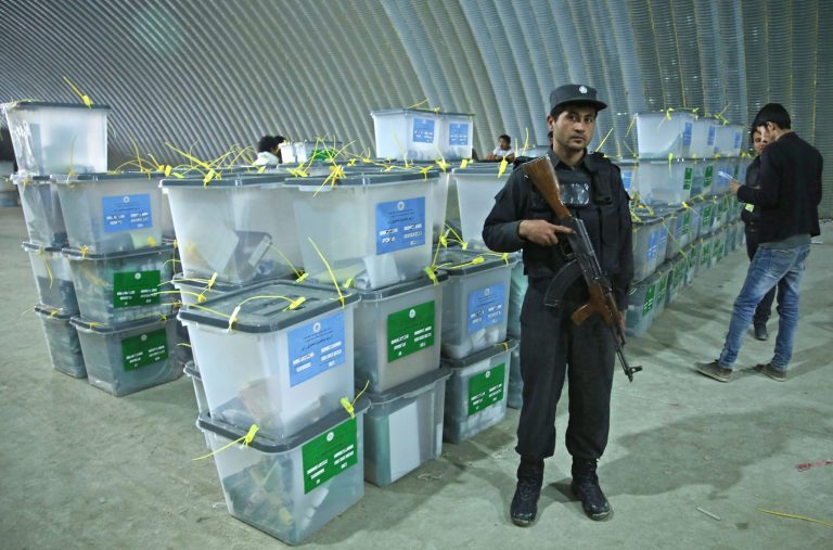 An Afghan police officer stands guard as Afghan election workers, right, note serial numbers of ballot boxes at a warehouse of the Independent Elections Commission warehouse in Kabul, Afghanistan, Sunday, April 6, 2014. Trucks and donkeys loaded with ballot boxes made their way to counting centers on Sunday as Afghans and the international community sighed with relief that national elections were held without major violence despite a Taliban threat. (AP Photo/Massoud Hossaini)