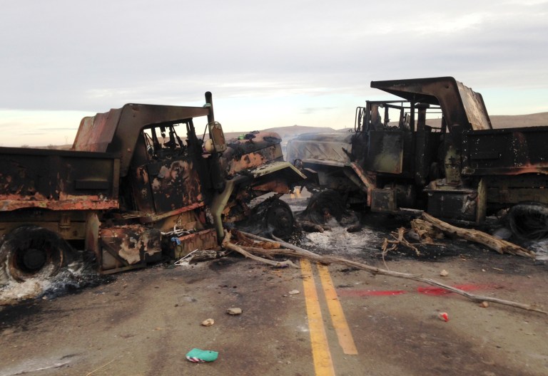 The burned hulks of heavy trucks sit on Highway 1806 near Cannon Ball, N.D., on Friday, Oct. 28, near the spot where protesters of the Dakota Access pipeline were evicted from private property a day earlier. Authorities say they have received little federal help to calm protests despite repeated requests. (AP Photo/James MacPherson)