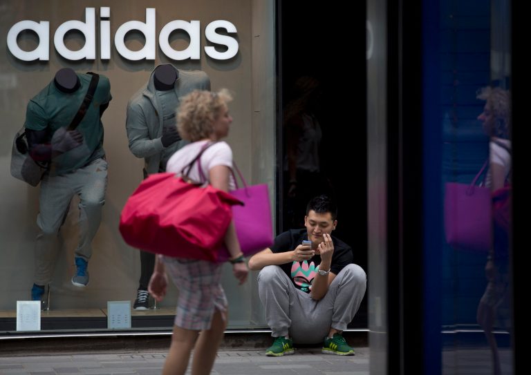 A shopper walks past a man smoking outside a sportswear outlet at a shopping mall in Beijing Monday, May 5, 2014. China's manufacturing contracted in April for the fourth straight month but the pace of decline was less severe, suggesting the downturn in the world's No. 2 economy is bottoming out. (AP Photo/Andy Wong)