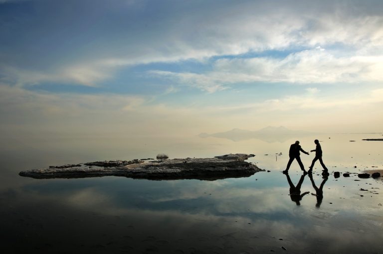 In this Saturday, Feb. 15, 2014 photo,  two men walk toward salt-covered rocks that were once deep underwater at Lake Oroumieh, in northwestern Iran. Oroumieh, one of the biggest saltwater lakes on Earth, has shrunk more than 80 percent to 1,000 square kilometers (nearly 400 square miles) in the past decade, mainly because of climate change, expanded irrigation for surrounding farms and the damming of rivers that feed the body of water, experts say. (AP Photo/Ebrahim Noroozi)