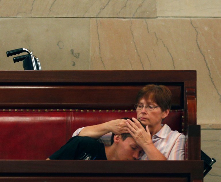 Rose Homuth of Cuba, N.Y., holds her son Brady Homuth, 25, in the Senate gallery at the Capitol as senators debate the medical marijuana bill on Friday, June 20, 2014, in Albany, N.Y. The Senate passed the bill making New York the 23rd state to legalize, but the drug won't be available for at least 18 months while regulations are written and five state-approved producers and distributors are chosen. Brady suffers from retractable seizure disorder. (AP Photo/Mike Groll)
