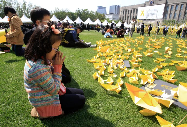 A girl prays in front of paper ships bearing messages for the victims of the sunken ferry Sewol at a group memorial altar in Seoul, South Korea, Monday, May 5, 2014. More than 300 people are dead or missing in the water off the southern coast in the disaster that caused widespread grief, anger and shame. (AP Photo/Ahn Young-joon)