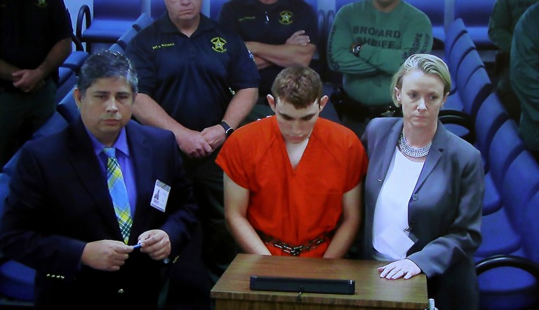 A video monitor shows school shooting suspect Nikolas Cruz, left, with public defender Melisa McNeill, making an appearance before Judge Kim Theresa Mollica in Broward County Court, Thursday, Feb. 15, 2018, in Fort Lauderdale, Fla. Cruz is accused of opening fire Wednesday at the school killing more than a dozen people and injuring several others. (Susan Stocker/South Florida Sun-Sentinel via AP, Pool)