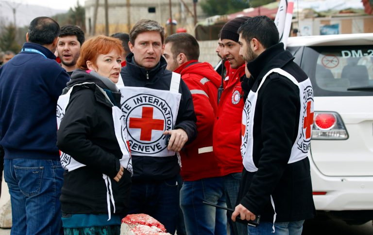 In this Monday, Jan. 11, 2016 photo, aid workers stand near a convoy of vehicles loaded with food and other supplies organized by the International Committee of the Red Cross, working alongside the Syrian Arab Red Crescent and the United Nations, makes it's way to the besieged town of Madaya, about 15 miles (24 kilometers) northwest of Damascus, Syria. Madaya has been blockaded for months by government troops and the Lebanese militant group Hezbollah. Opposition activists and aid groups have reported several deaths from starvation in recent weeks. (AP Photo)