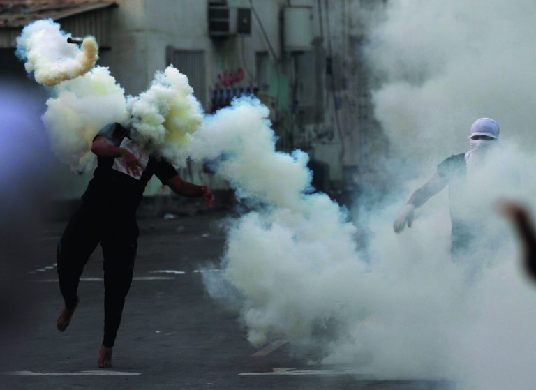 A Bahraini anti-government protester throws a tear gas canister back toward riot police who fired it during clashes after the politically charged funeral for a teenager in Muharraq, Bahrain, on Saturday, Nov. 10, 2012. Bahrain's main opposition group says the kingdom's paramilitary national guard is deploying to back up police as authorities try to quell rising political violence. (AP Photo/Hasan Jamali)